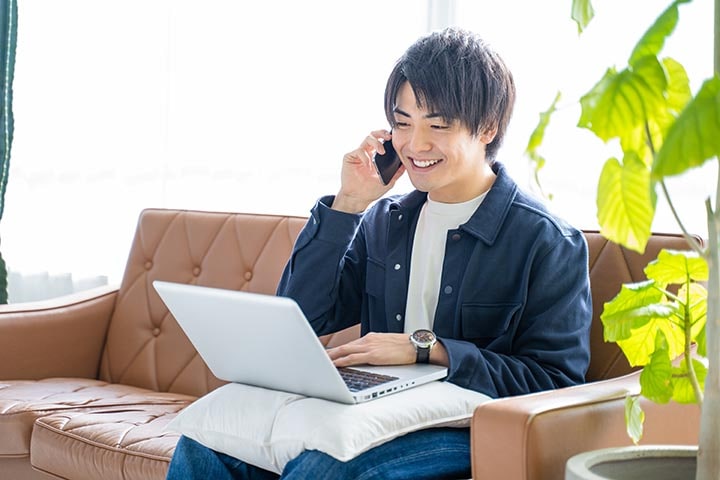 ソファで電話しながら笑顔の男性